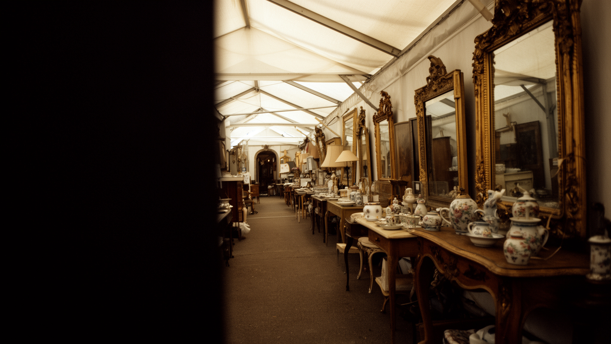 Grande allée d'une exposition-vente parisienne à l'aube, cadres dorés et grès alignés sous une lumière basse
