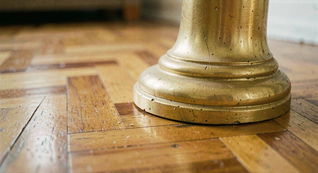 Détail d'un pied doré mouluré devant un parquet ciré